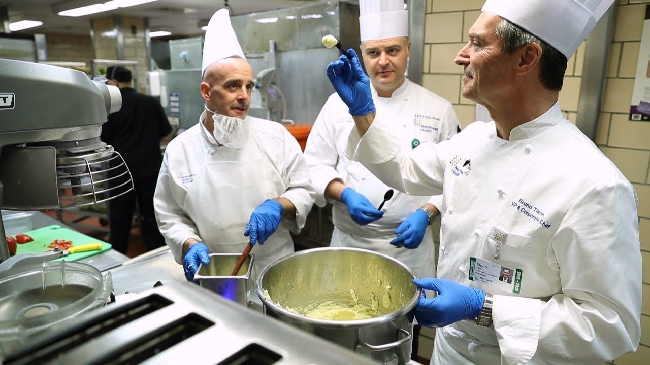 Three male chefs standing in a restaurant kitchen in front of a pot on the stove.