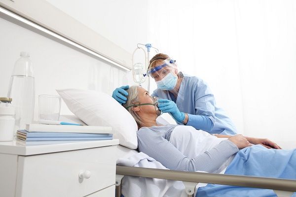 A nurse is putting an oxygen mask on an elderly woman in a hospital bed.