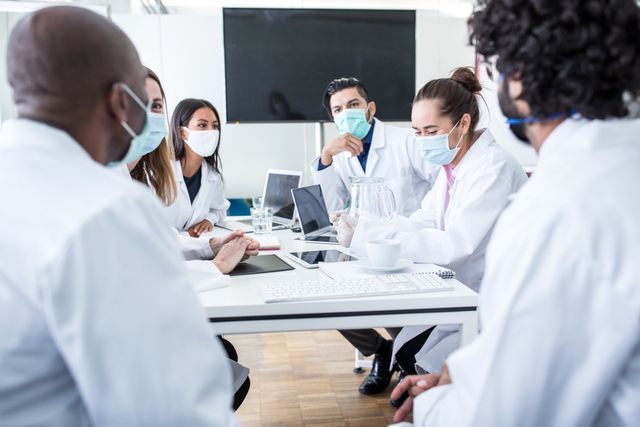 a group of doctors wearing face masks are having a meeting .
