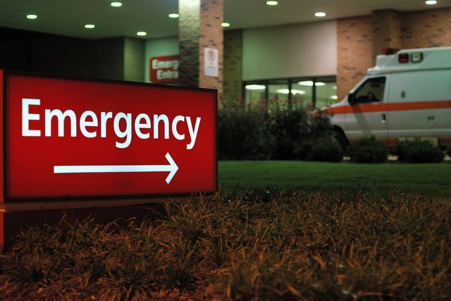 an emergency sign in front of a hospital with an ambulance in the background .
