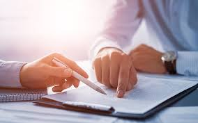 Hands pointing to a document during a meeting, with a pen, watch, and sunlight in the background.