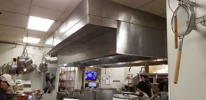 A kitchen with stainless steel appliances and pots and pans hanging from the ceiling.