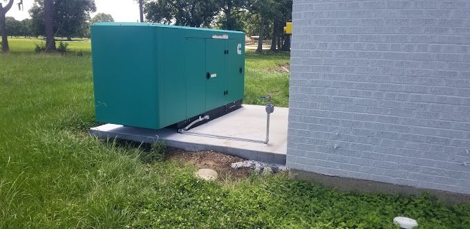 A green box is sitting in the grass next to a brick building.