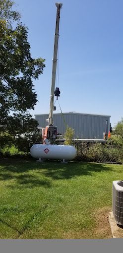 A large propane tank is being lifted by a crane.