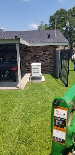 A green tractor is parked in front of a house with a generator in the backyard.