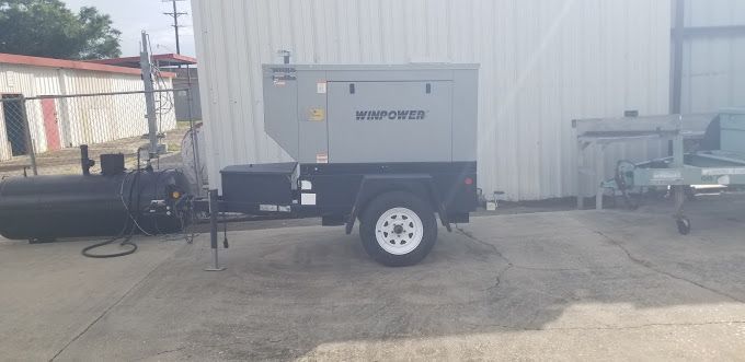A trailer with a generator attached to it is parked in front of a building.