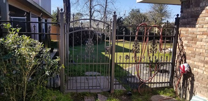 A wrought iron gate is leading to a lush green yard.