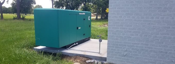 A green generator is sitting next to a brick building in a grassy field.