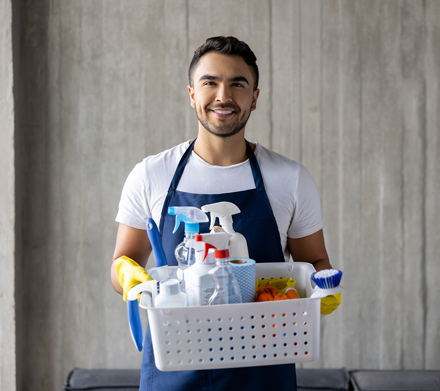 A man in an apron is holding a basket full of cleaning supplies.