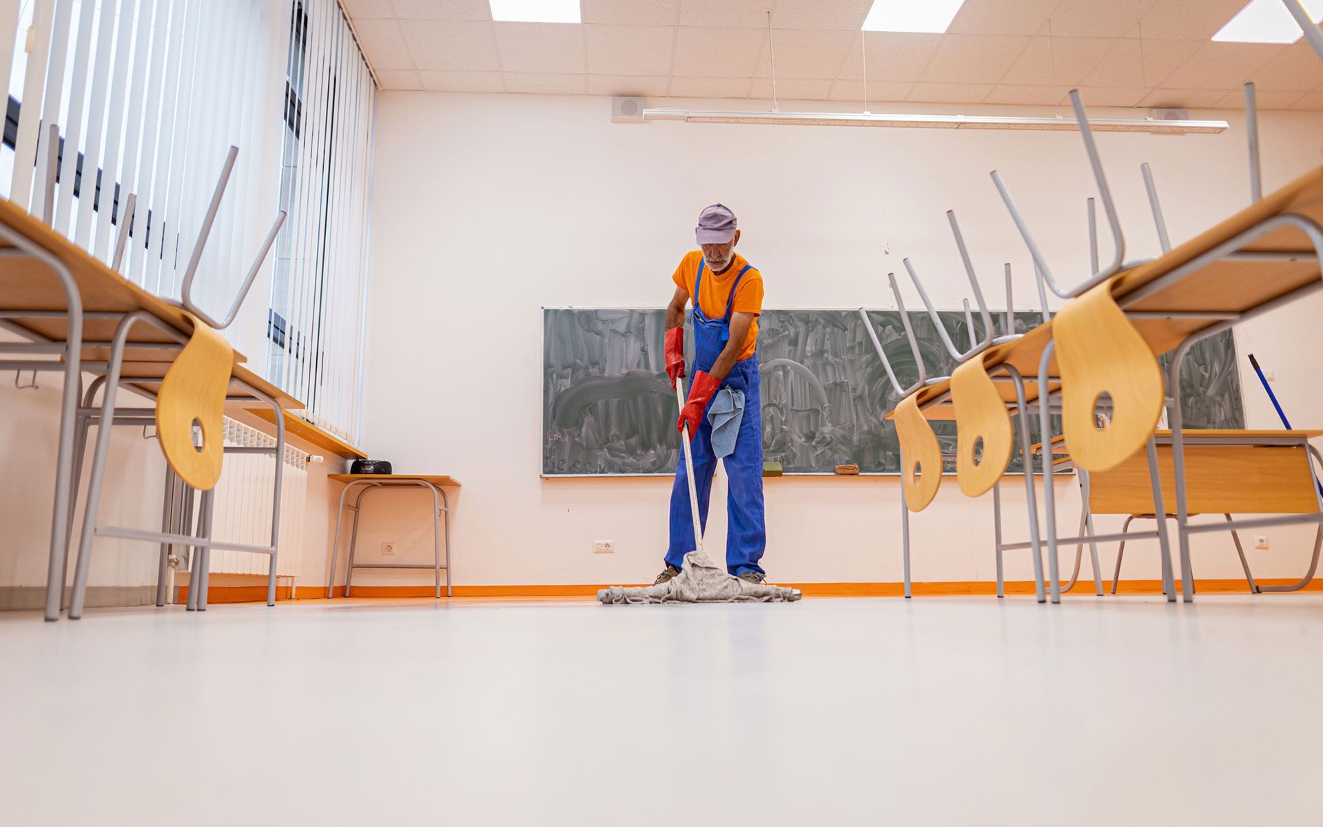A man is cleaning the floor of a classroom with a mop.