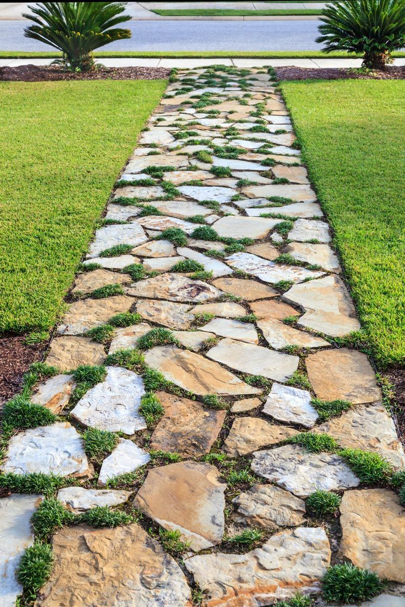 Stone pathway with grass growing between stones, flanked by green lawns.