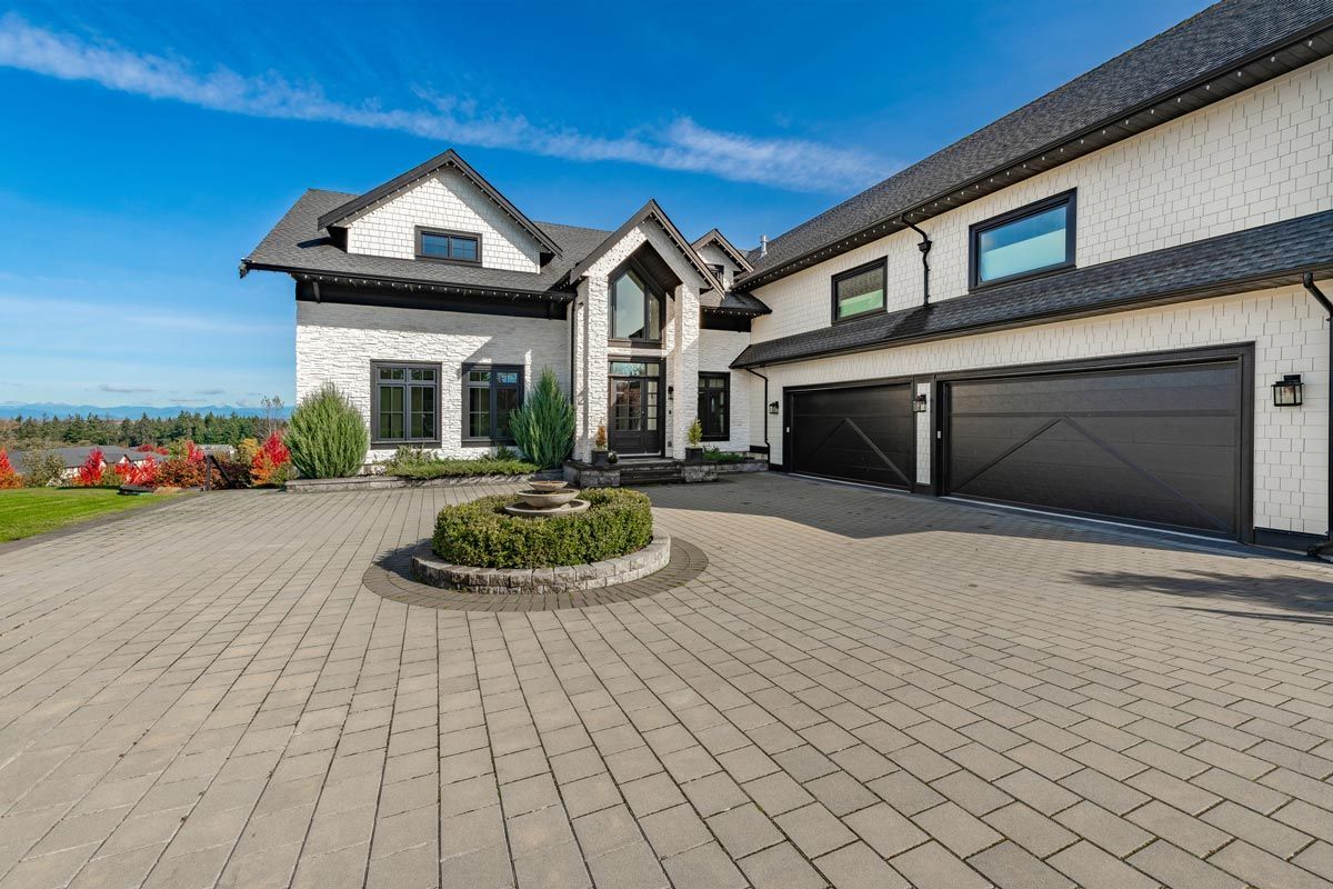 Two-story white house with black trim, black garage doors, and brick driveway under blue sky.