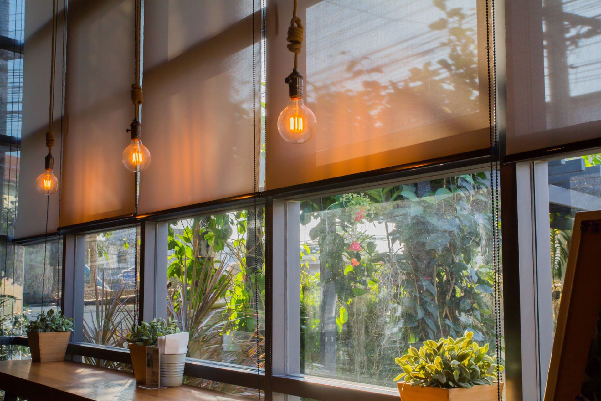 Warm café interior with hanging lights, large windows, and potted plants near a counter — Another Blind Man in Tewantin, QLD