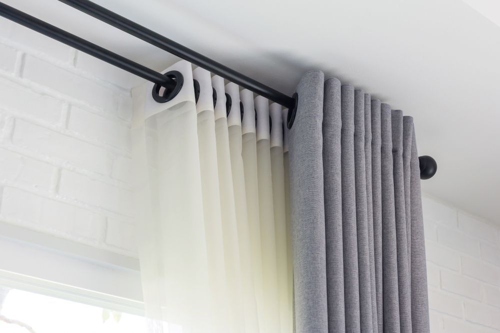 Sheer white and grey curtains on a black curtain rod beside a white brick wall and window — Another Blind Man in Tewantin, QLD
