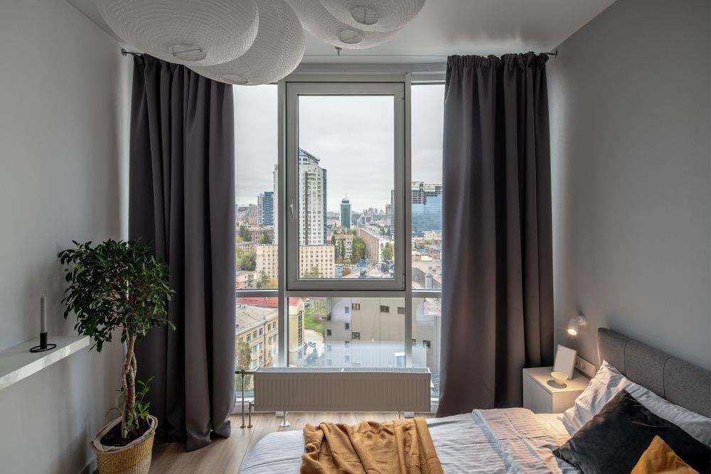 Modern bedroom with large window, grey curtains, city view, and a bed with mustard blanket — Another Blind Man in Tewantin, QLD