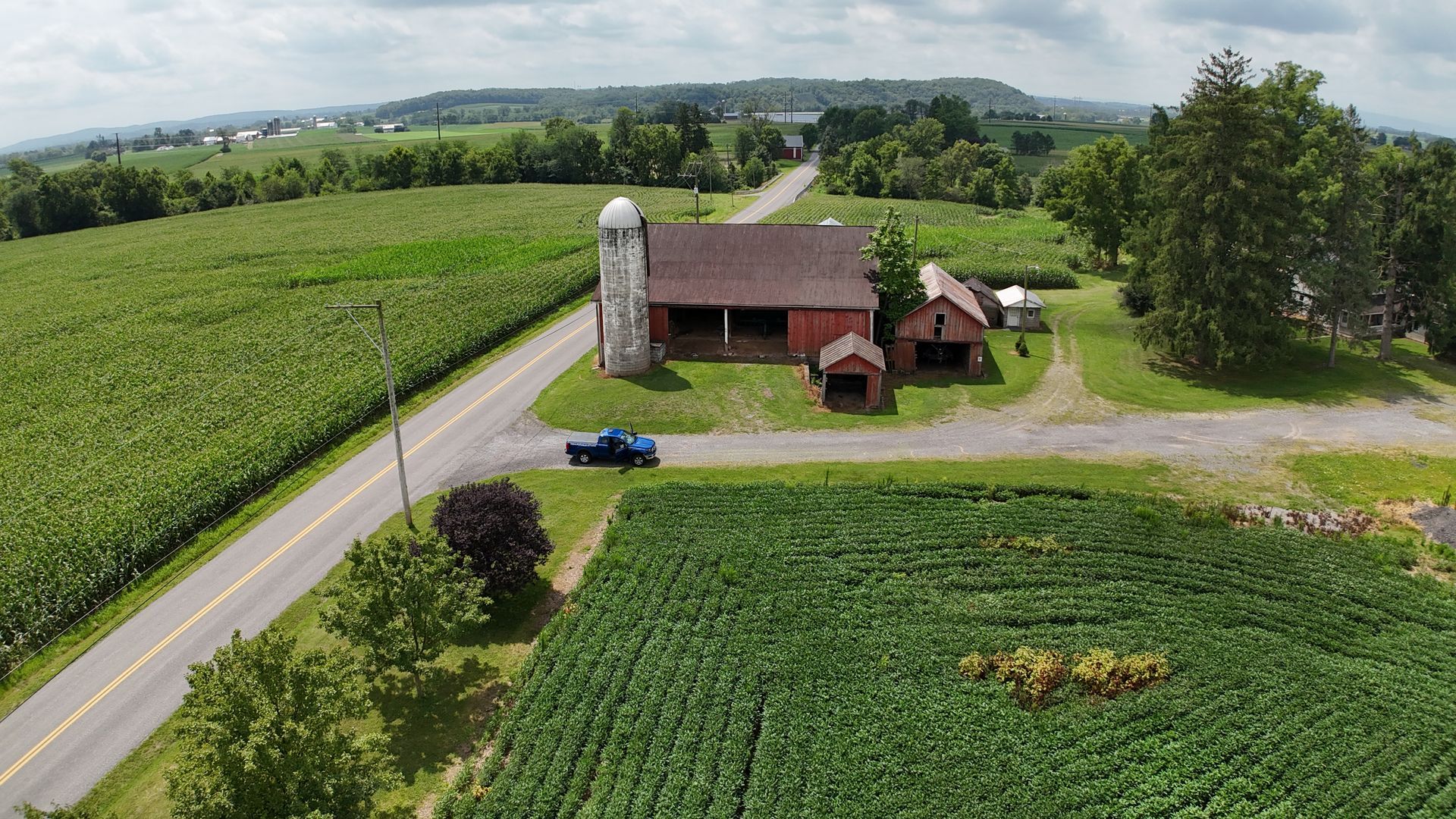 Aerial view of a farm with a red barn, silo, green fields, and a rural road, highlighting a classic ranch building setting.