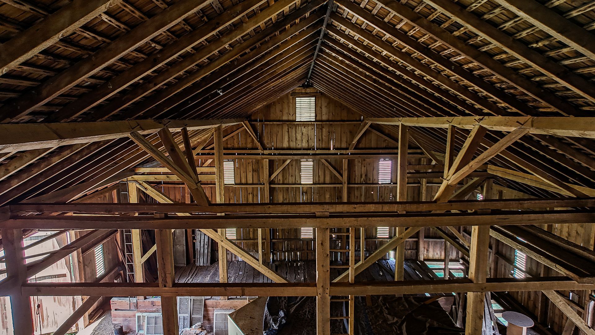 The inside of a barn with wooden beams and a roof.