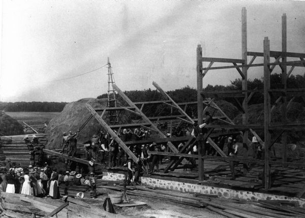 A black and white photo of a barn under construction.