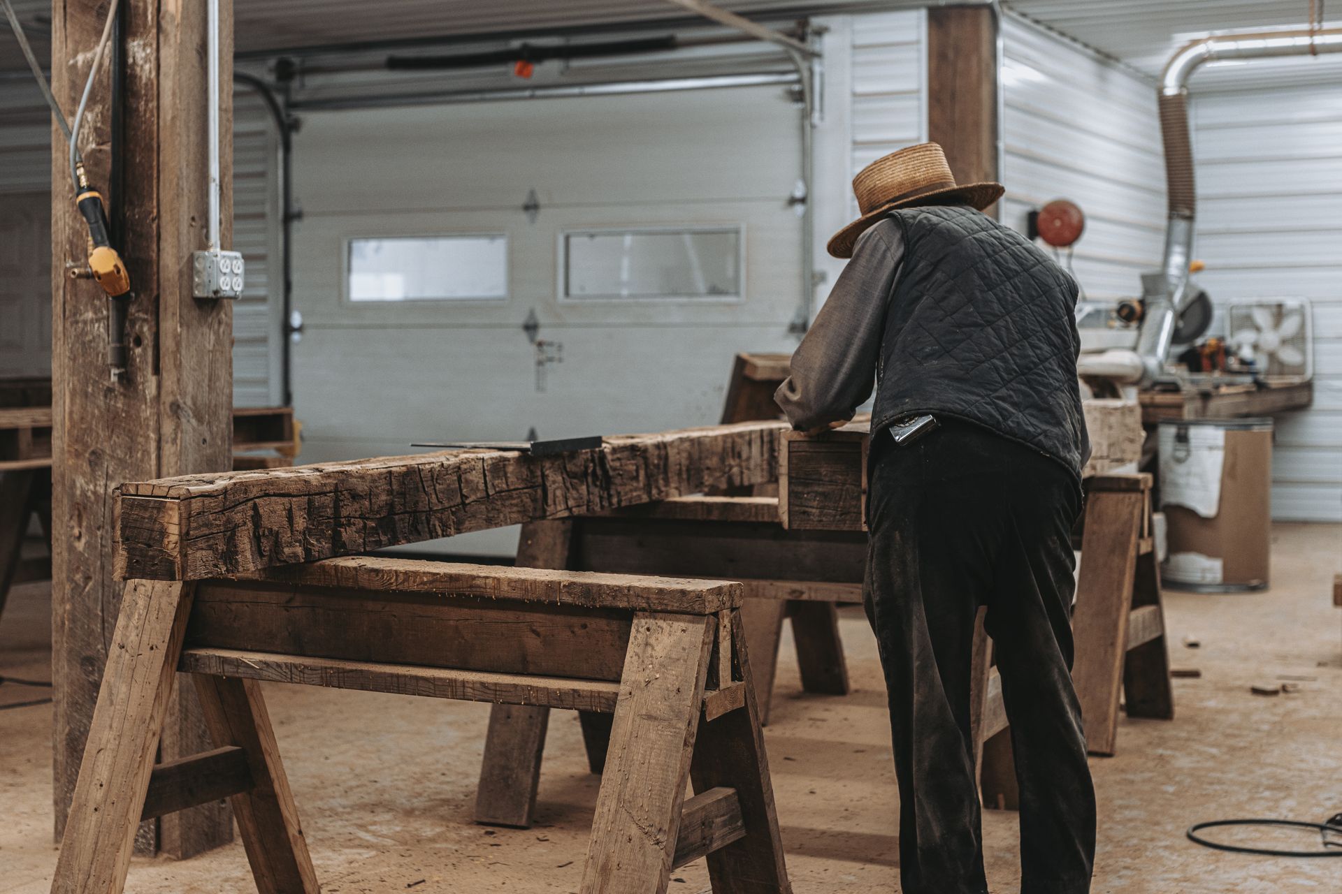 A man in a straw hat is working on a piece of wood in a workshop.