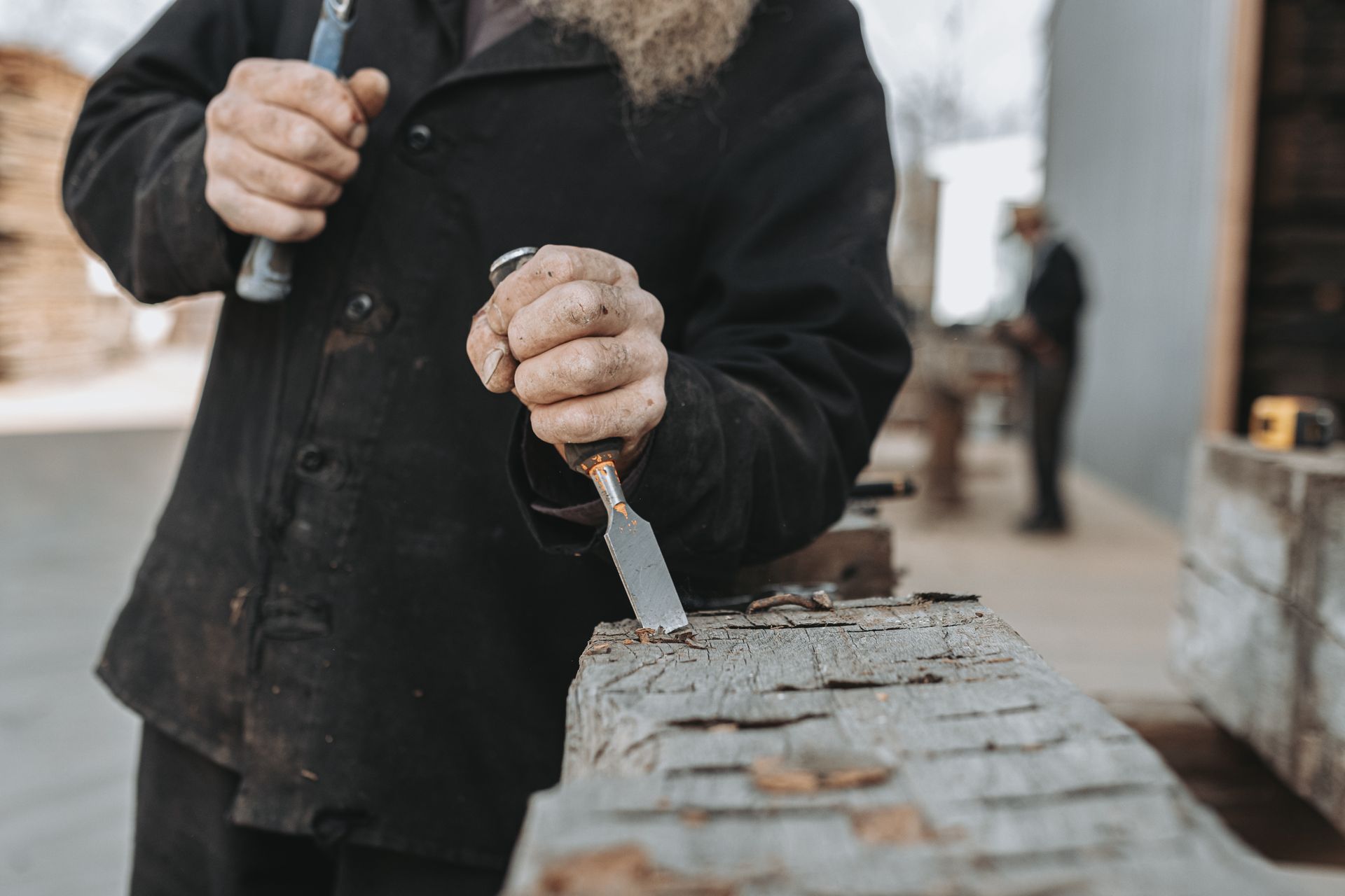 A man with a beard is carving a piece of wood with a spatula.