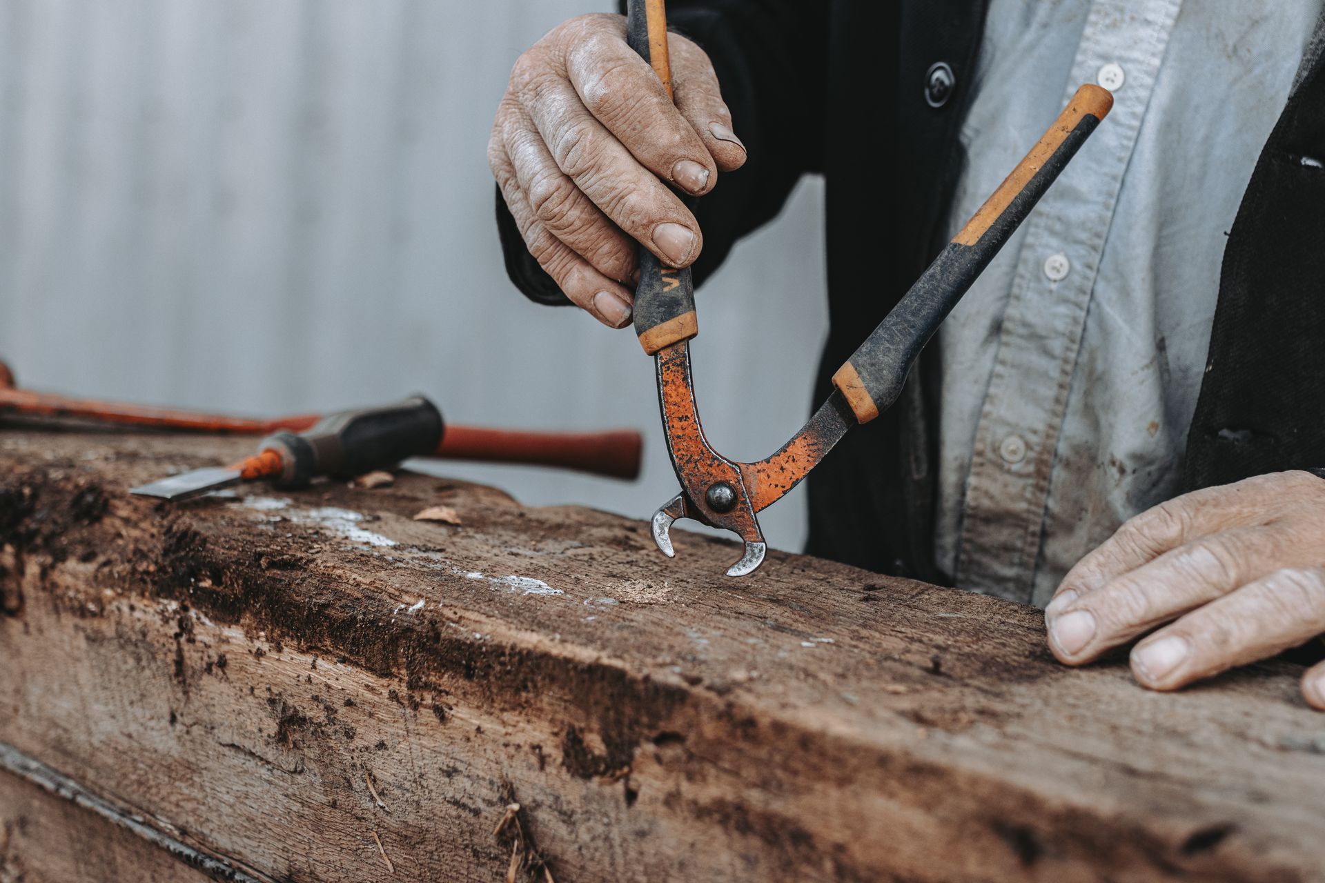 A man is holding a pair of pliers over a piece of wood.