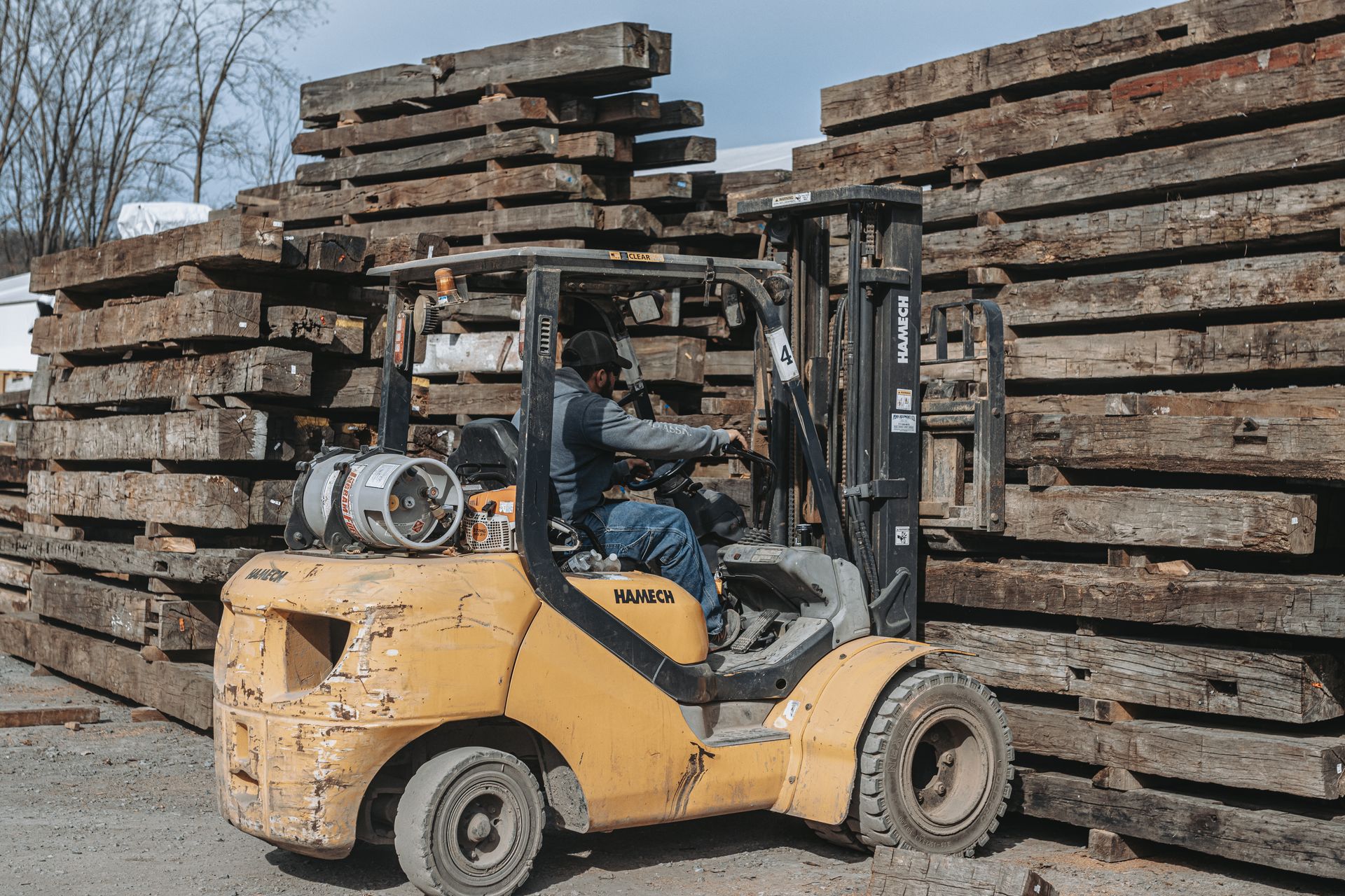 Yellow forklift in a lumber yard with weathered beams which were party of the antique barn dismantling service.