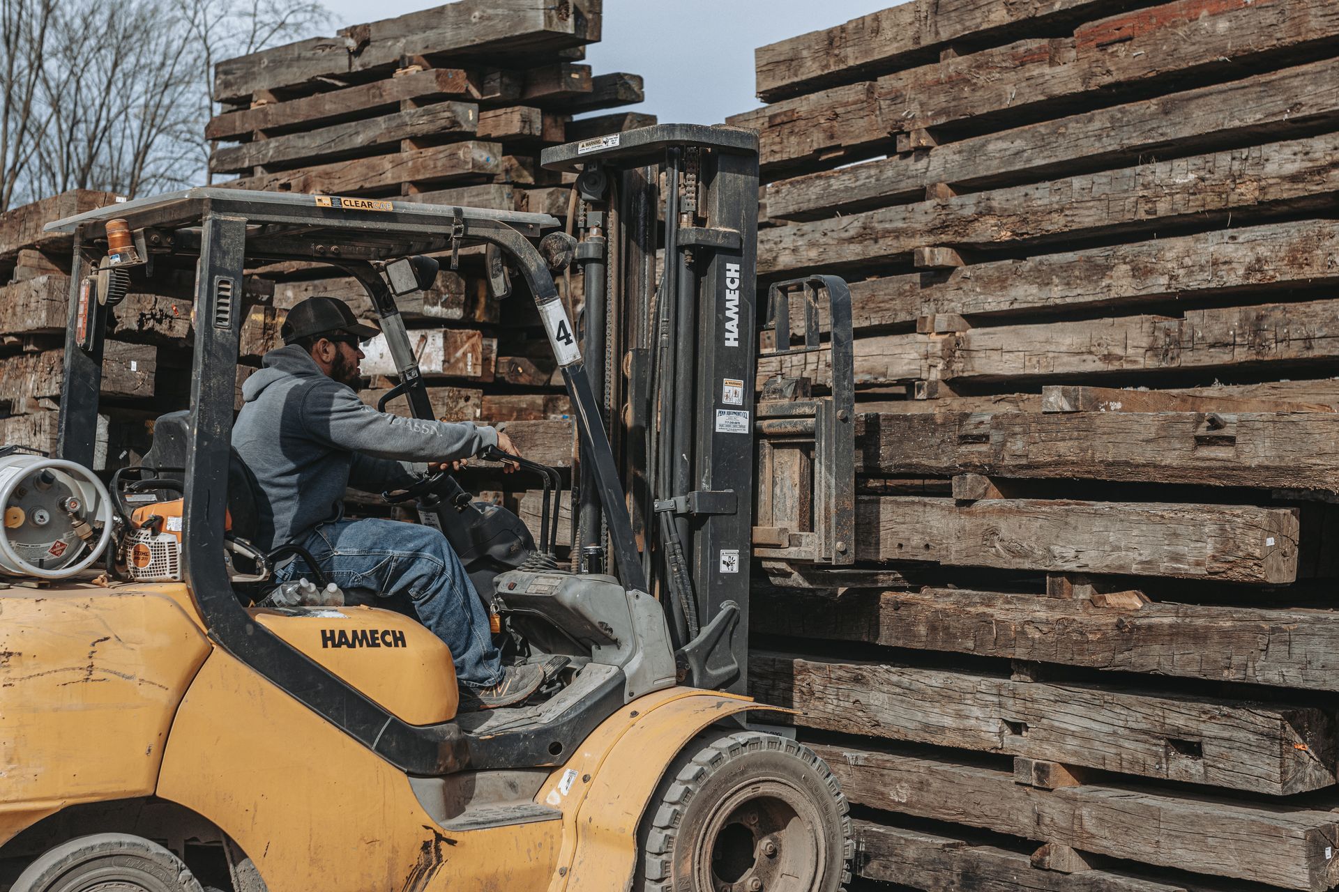 Forklift operator moving stacks of old timbers in a lumberyard.