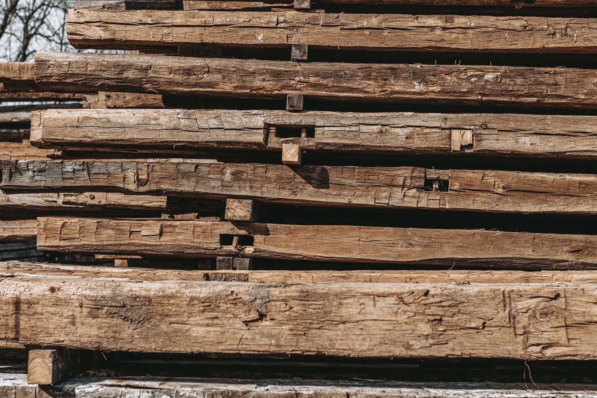 Stack of weathered wooden beams with visible joinery for heritage timber frame restoration.