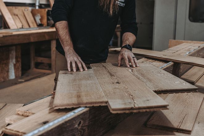 A man is standing next to a pile of wood in a workshop.