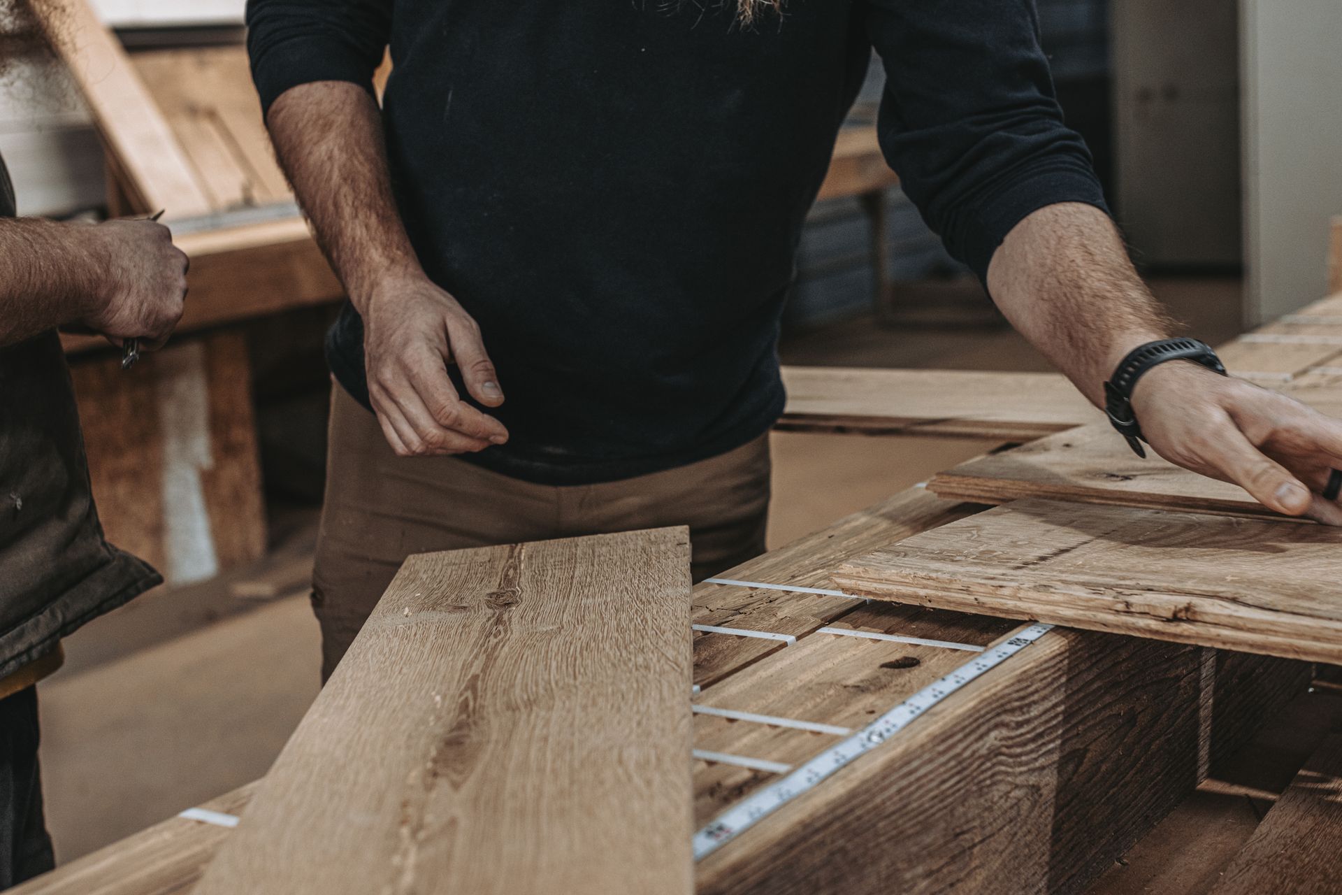 Craftsmen measuring softwood planks in a workshop.