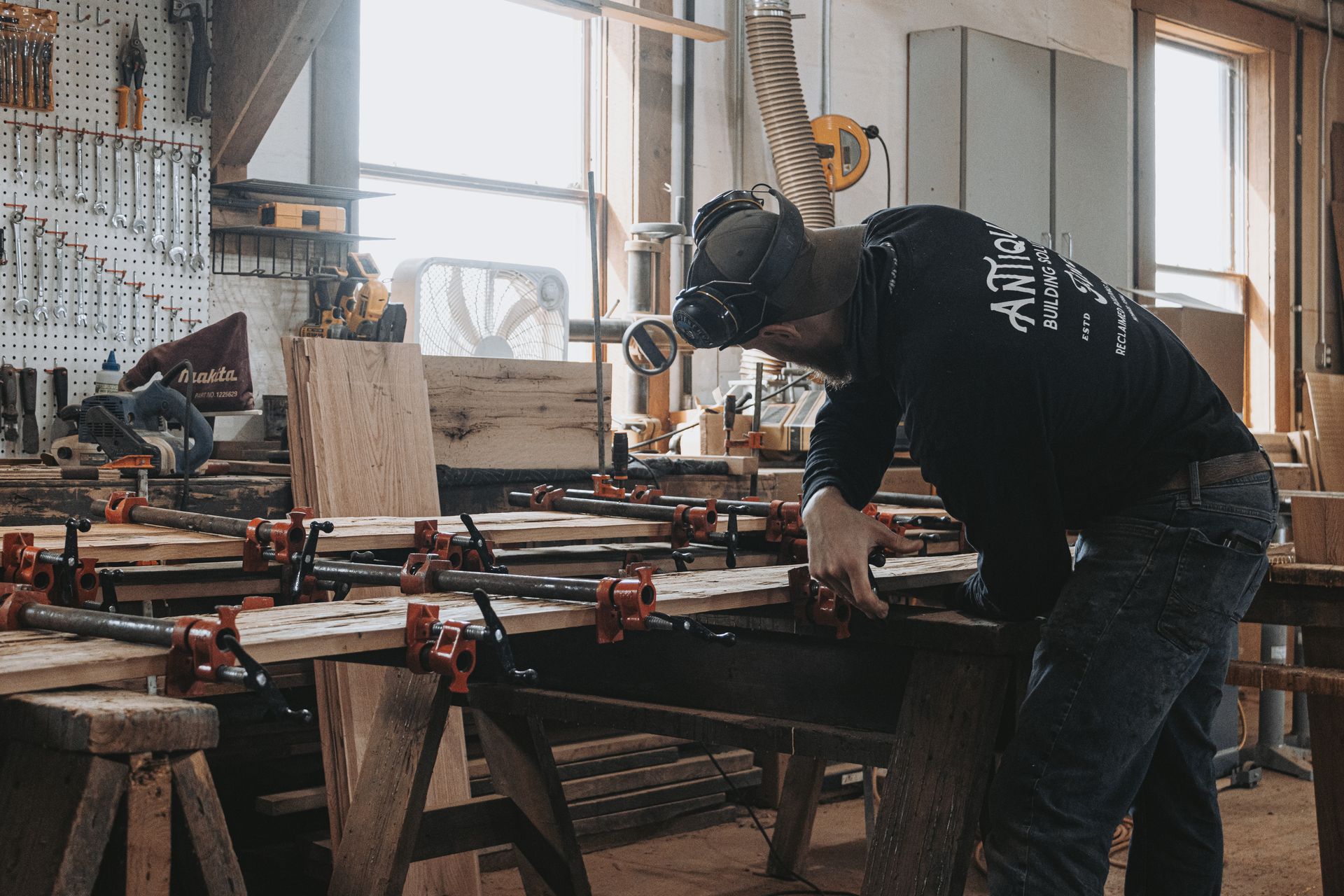 A craftsman in a workshop clamps wooden boards together, part of the timber frame restoration process.
