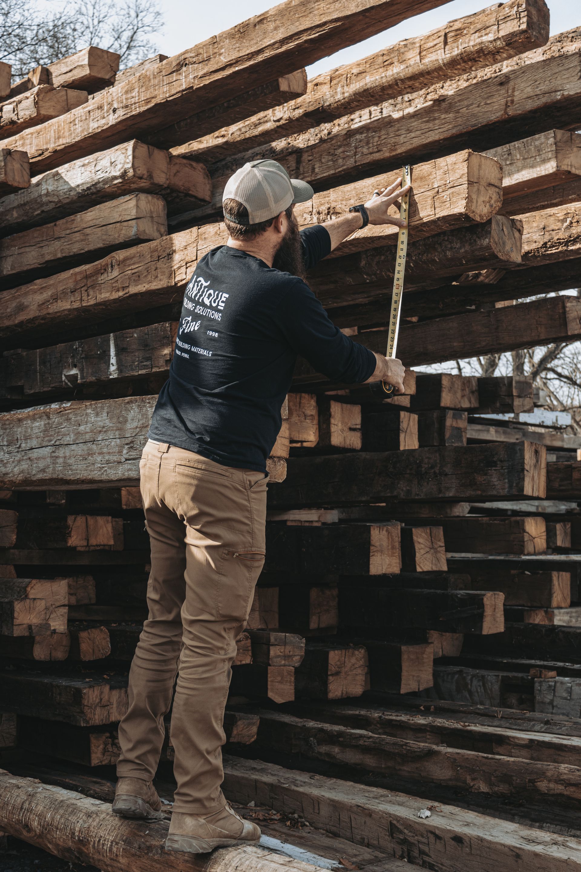 A man is standing on top of a pile of wooden beams holding a hammer.