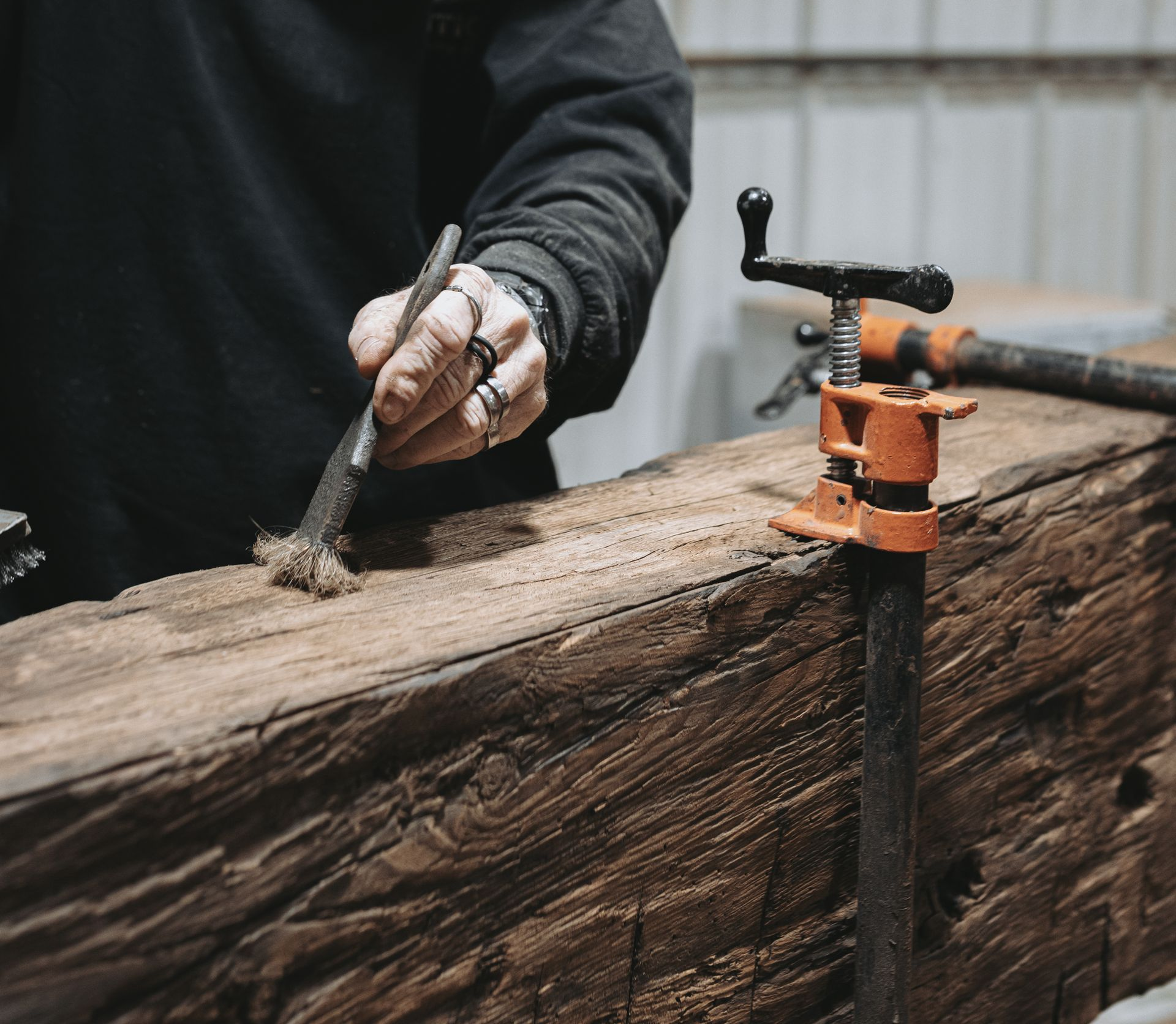 In Pennsylvania, a hand applies wood conditioner to aged beam highlighting preservation and care. 