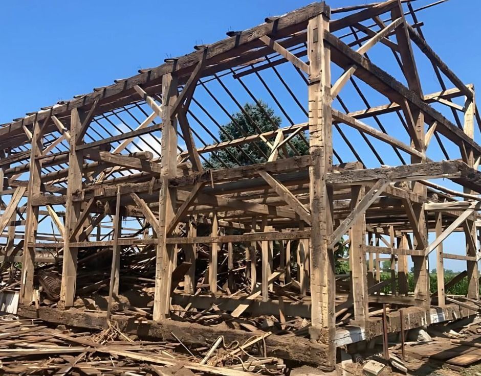 A weathered, Exposed barn frame salvage amidst debris.