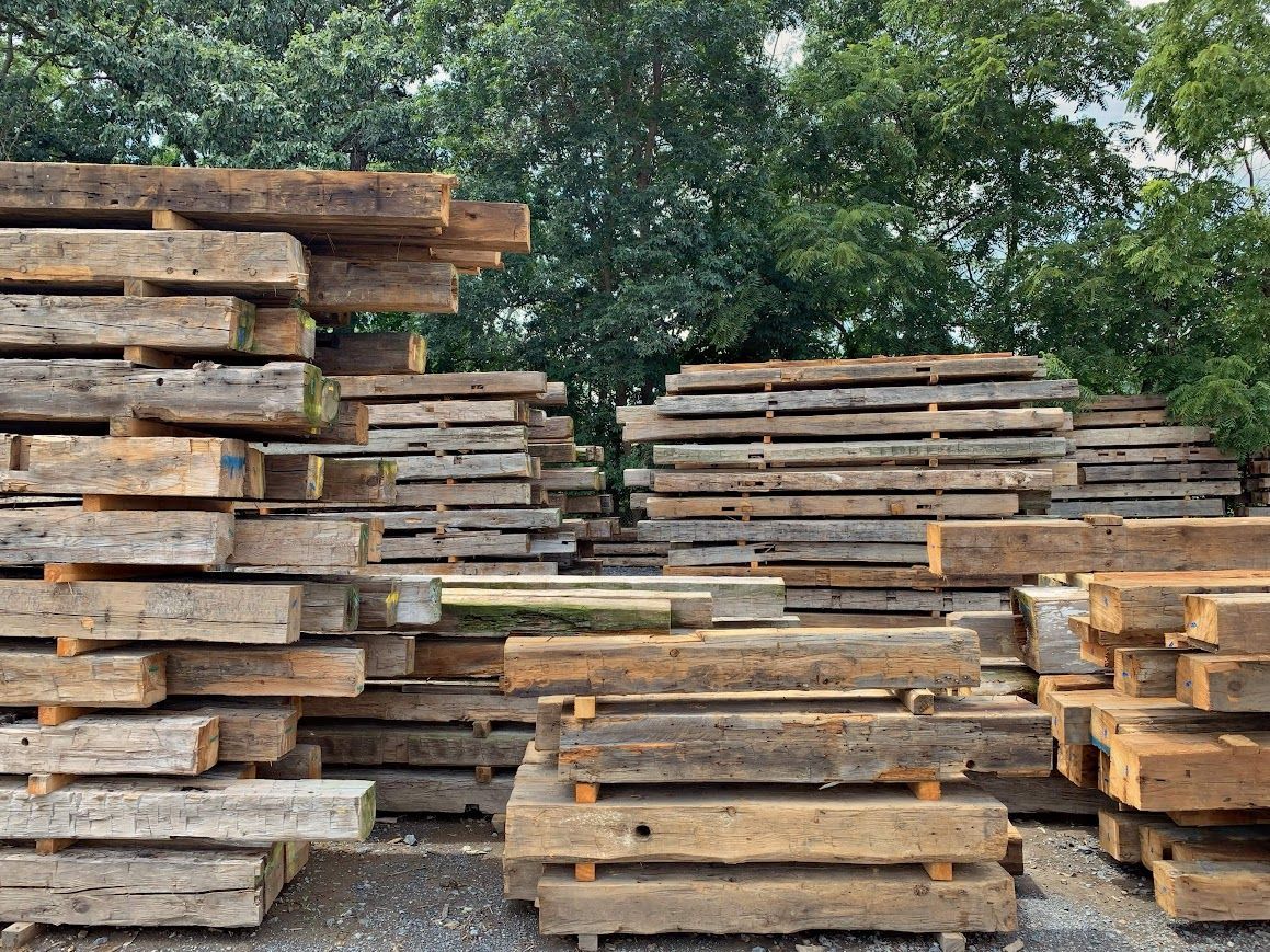 Stacks of reclaimed wooden beams outdoors, from the best barn frame supplier.