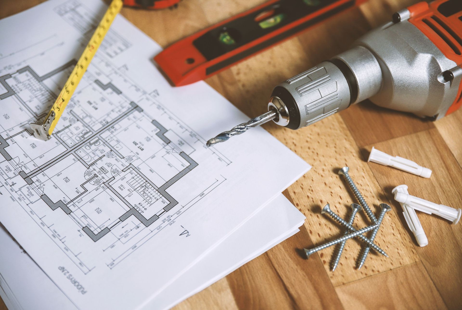 A drill is sitting on top of a house plan on a wooden table.