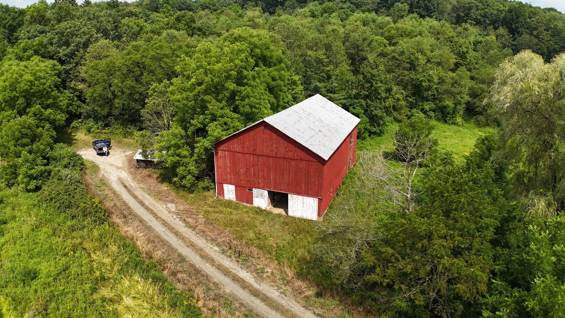 An aerial view of a red barn surrounded by trees and a dirt road.