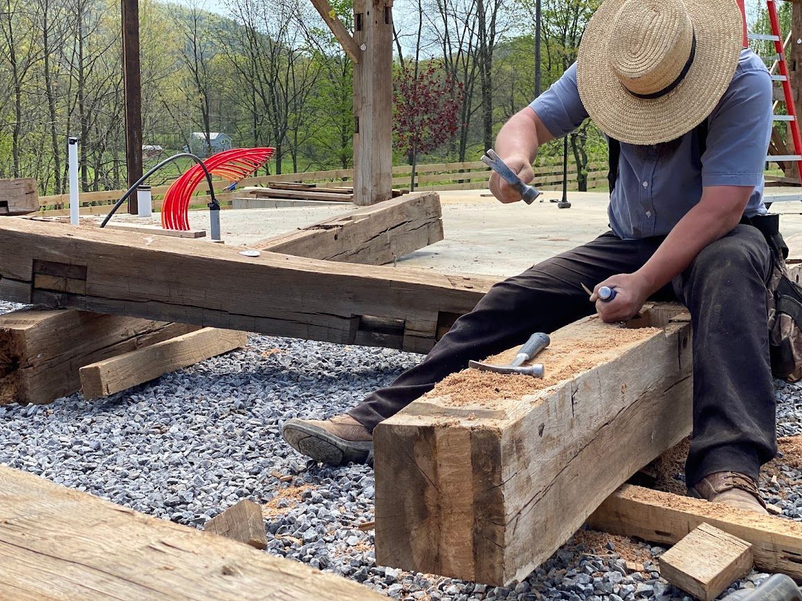 Craftsman shaping timber beams using green building techniques outdoors in Pennsylvania.