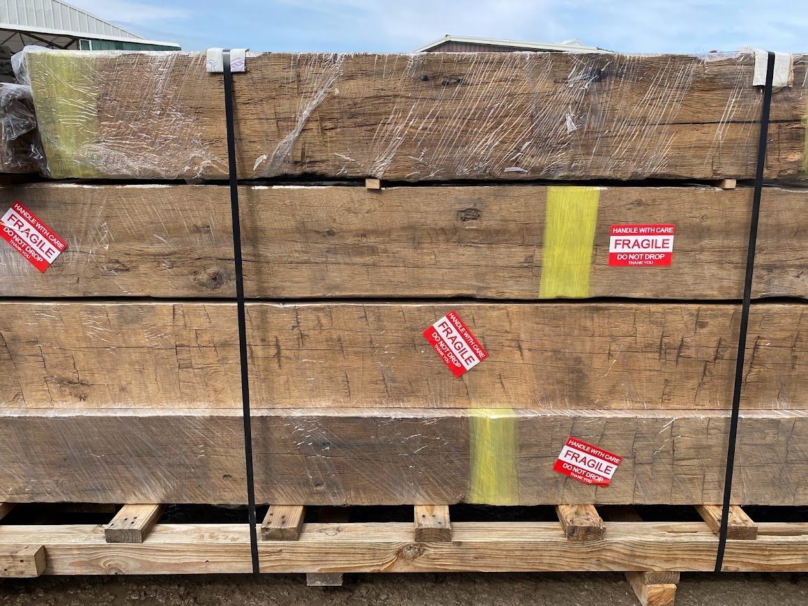 Stacked wooden beams prepared for antique barn frame delivery.