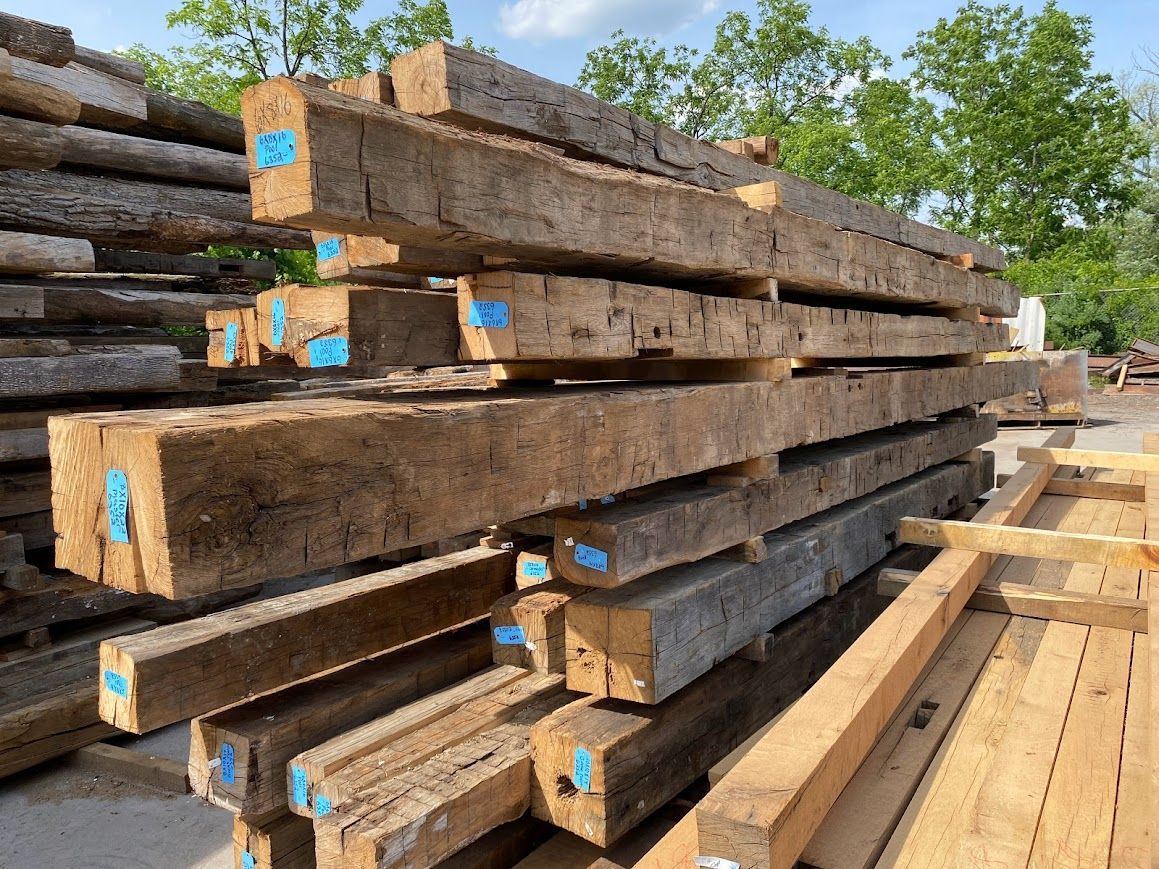 Stacked reclaimed wooden beams with tags, showcasing high-quality barn frames.