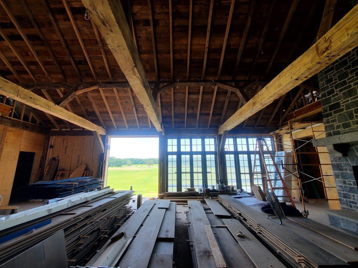 Interior of a barn under renovation with exposed beams, large windows, and barn to house conversion plans in progress.