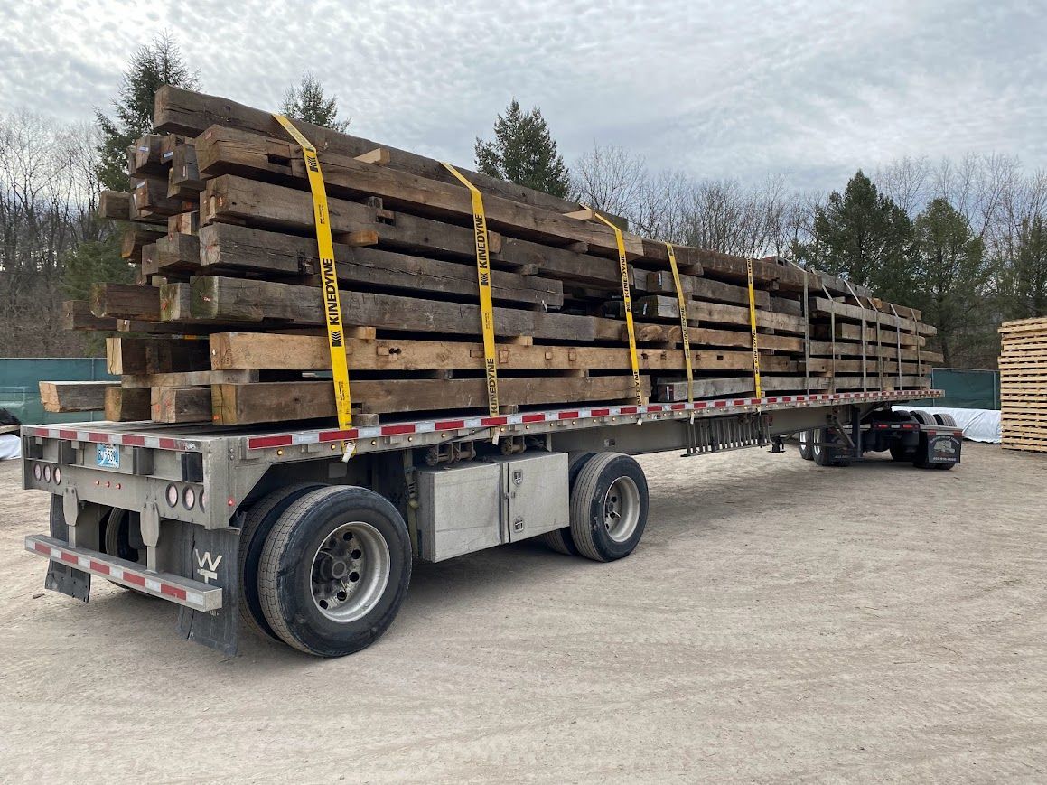Flatbed trailer loaded with reclaimed wooden beams, showcasing barn frame dismantling.