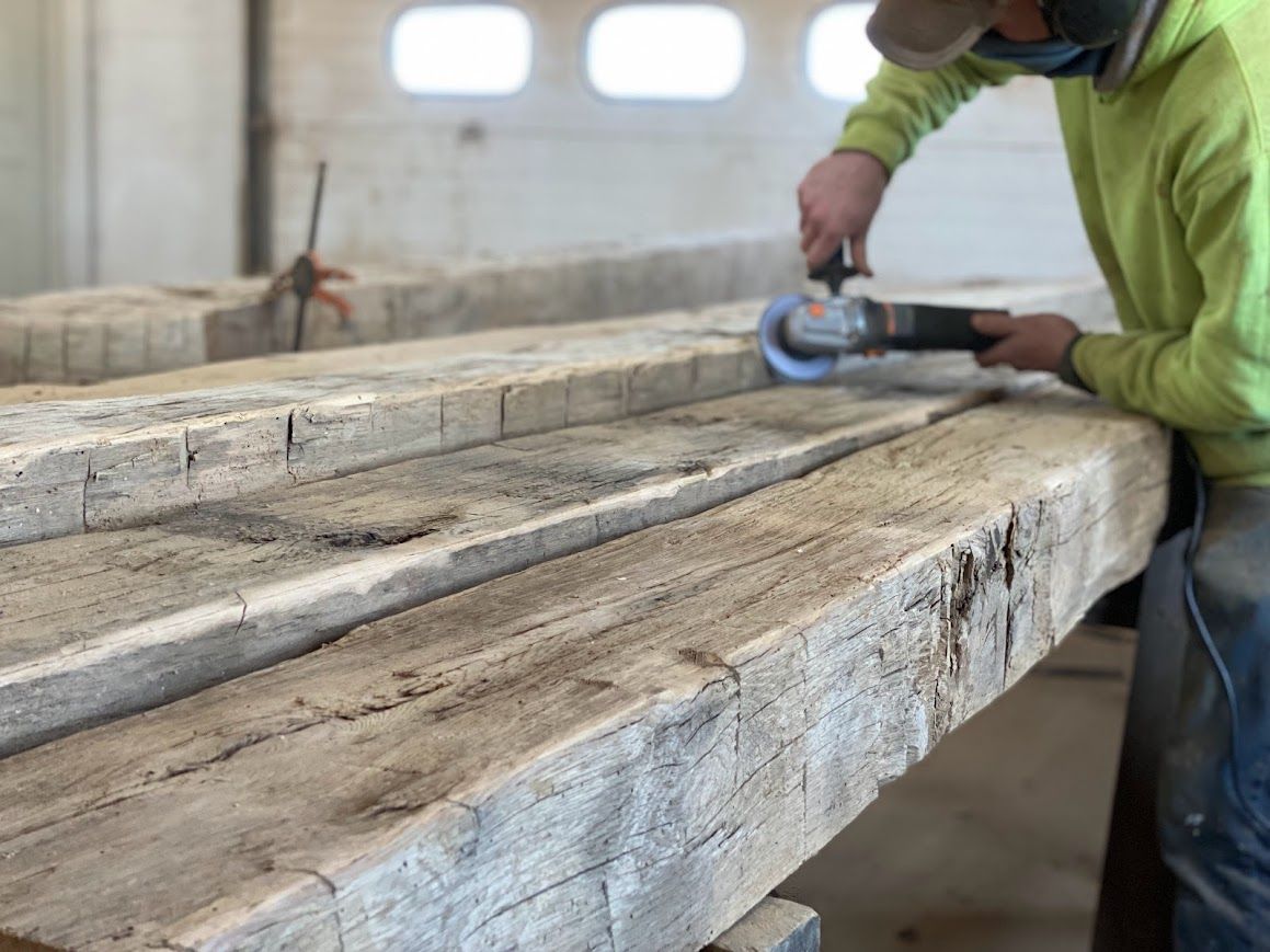 Worker sanding reclaimed wood, showcasing repair of barn frames.