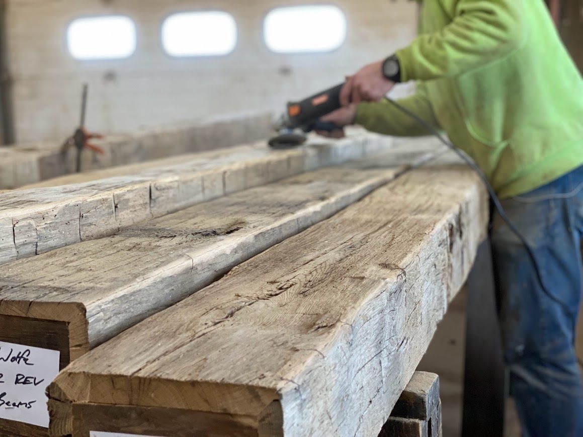 Timber frame barn beams being sanded in a workshop.