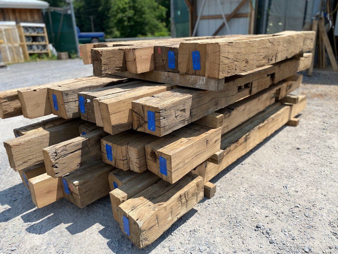 Timber frame barn beams stacked with blue inventory tags.