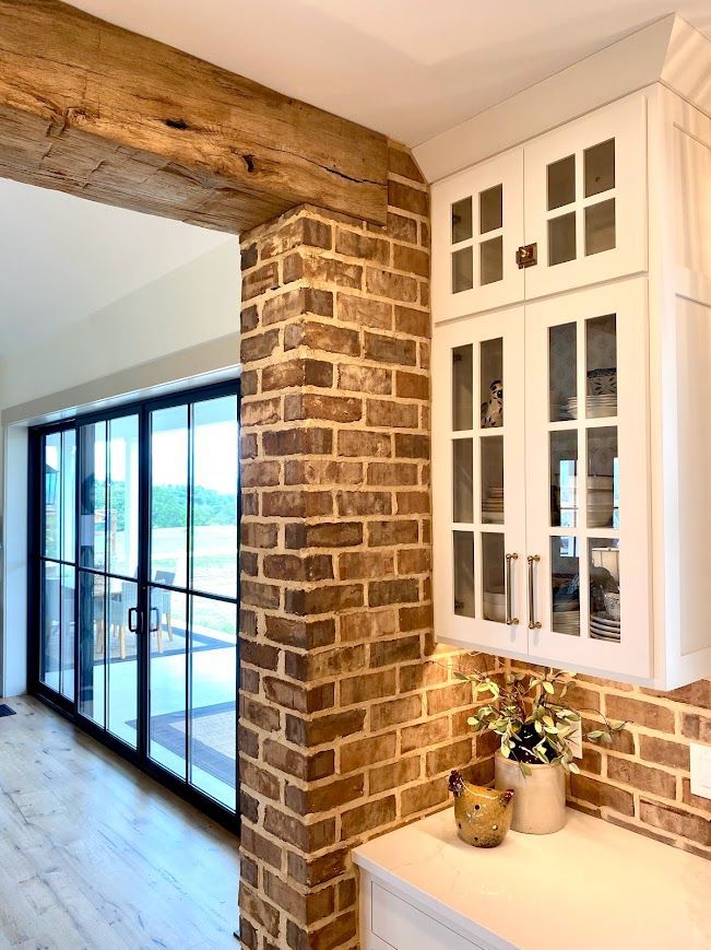 Modern farmhouse design with brick column, wooden beam, and glass doors.