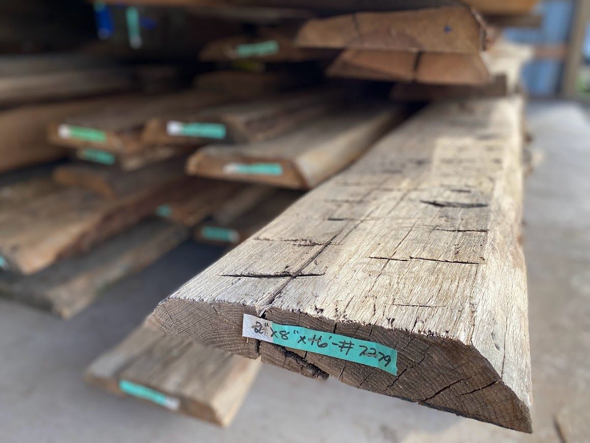Stack of labeled reclaimed wooden beams, ideal for sourcing historic barn structures.