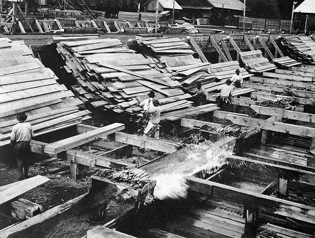 Workers guiding old timbers through water channels at a historic lumber mill in Pennsylvania.