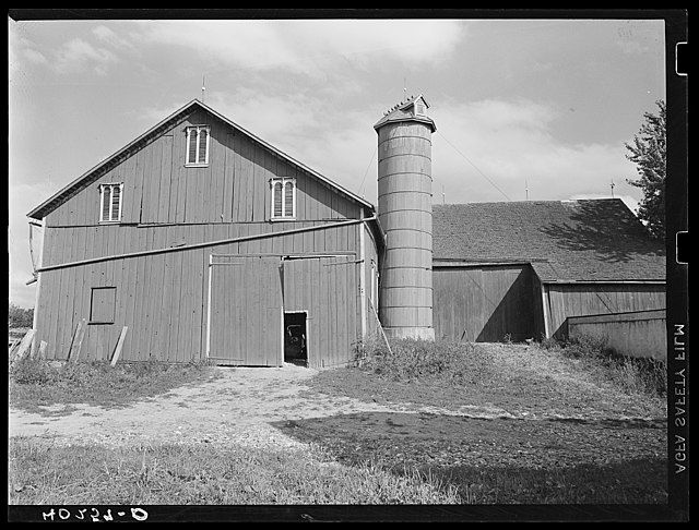 A black and white photo of a traditional barn and an adjacent silo, representing barns of America.
