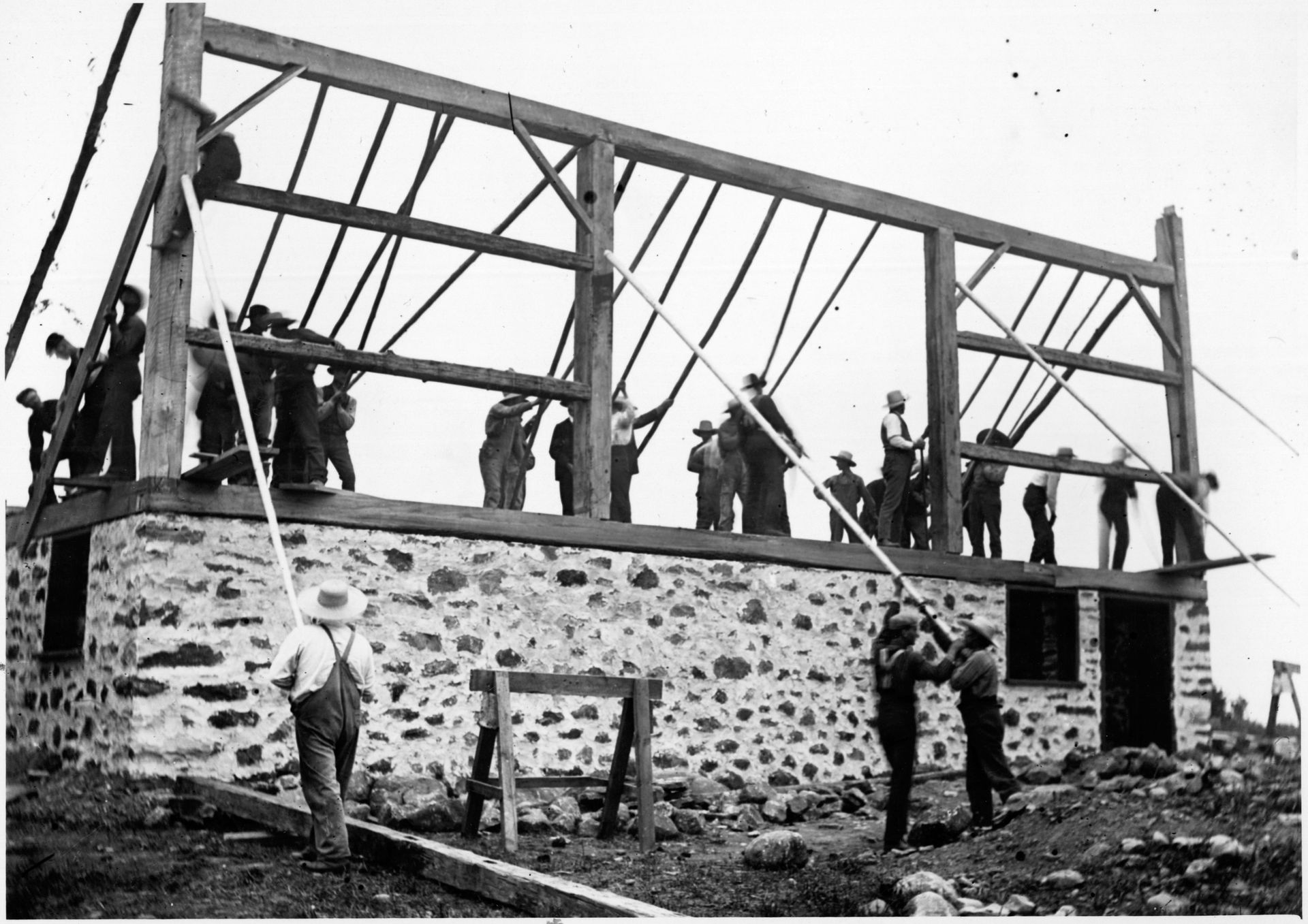 A historic black and white photo of a group of men building a barn 